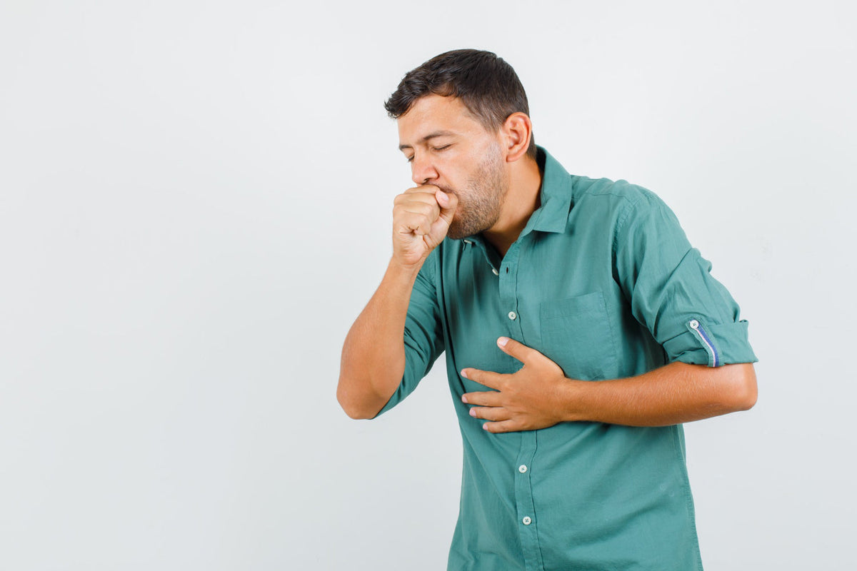 Man in a green shirt coughing into his fist with his other hand pressed to his chest